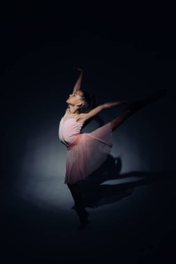Pembe elbiseli balerin kız dans eder ışıkla aydınlatılır karanlık arka planda.