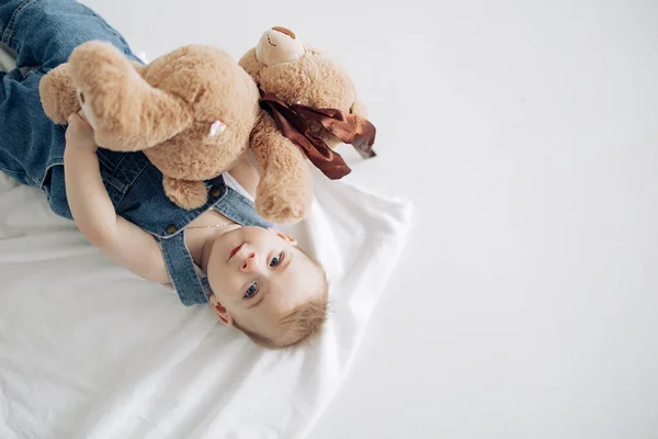 かわいい赤ちゃんの男の子が床に横たわっておもちゃのぬいぐるみクマと遊ぶ コピースペース付きの画像 トップ表示 — ストック写真