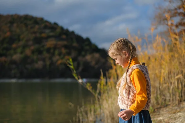 Küçük kız sonbahar kayalık çayırında taşlarla oynuyor. Anaokulu çocuğu açık bir sonbahar gününde ormanda yerde oturur. — Stok fotoğraf