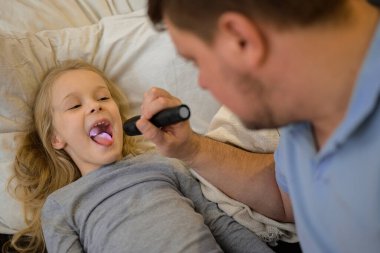 dad checks the throat of his sick child, shines a flashlight so that it is better to see. The father suspects that his daughter is ill. The child is not feeling well. the concept of equality in the