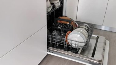 Bulaşık makinesini beyaz mutfakta temiz bulaşıklarla açın.