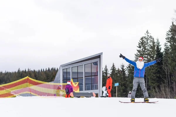 Un homme en chapeau de Père Noël avec un snowboard dans une station de ski. — Photo