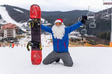 Kayak merkezinde kar kayağı yapan Noel Baba şapkalı bir adam.