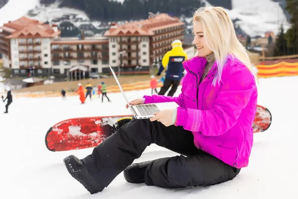 Frau sitzt mit Laptop auf einem Winterberg vor einer Hintergrundlandschaft — Stockfoto