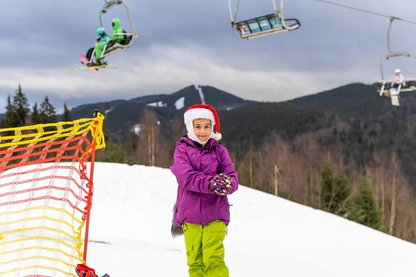 Klein meisje in santa hoed met snowboard in wintersportplaats — Stockfoto