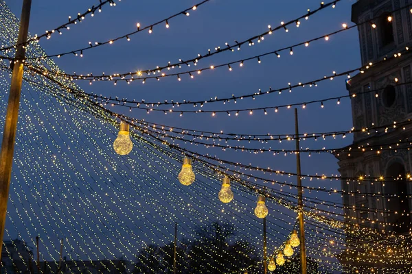 Elegante árbol iluminado con cálidas luces doradas, decoración festiva de calle o plaza. Árbol tronco y ramas en luces doradas bokeh en la noche. Feria de invierno de vacaciones. Feliz Navidad, espacio para copiar — Foto de Stock