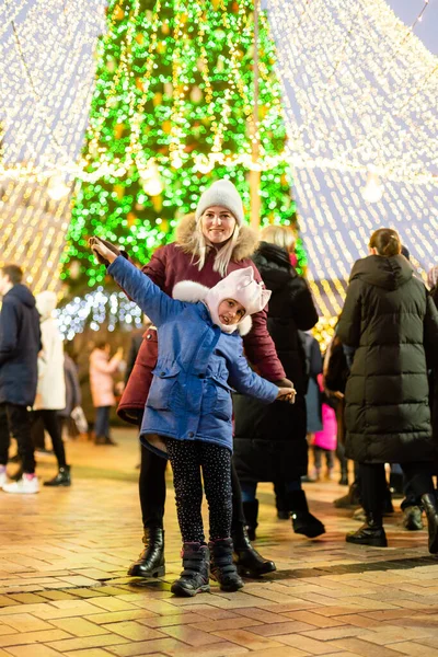 Anne ve kızı panayırdaki bir Noel ağacının önünde.