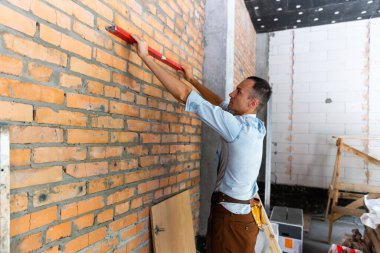 Boş dairede genç bir profesyonel. Ölçüm bandıyla duvarı ölçüyor, notları doğruluyor. Onarım ve yenileme konsepti