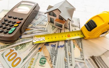 İnşaat planları, hesap makinesi, para ve kulübenin planı. Kendi evini geçindirmenin bedeli. Mülkün fiyatı. İpotek kredisi. Emlak kredisinin teminatı.