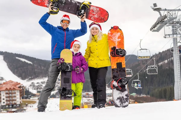 A szülők a lányukkal ünneplik a téli ünnepeket. család télapó kalap és snowboard téli üdülőhelyen — Stock Fotó