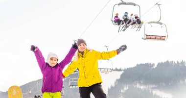 Snowboard yapan anne ve kızı karda oynuyorlar.