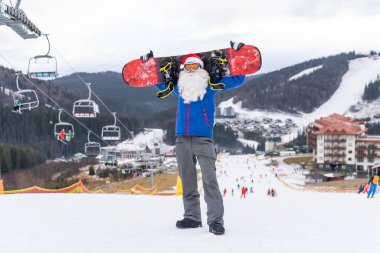 Kayak merkezinde kar kayağı yapan Noel Baba şapkalı bir adam.
