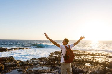 Genç ve çekici bir adam okyanusta duruyor ve kumsaldaki durumu kontrol ediyor. Okyanus dalgaları ve mavi gökyüzü arkaplanı