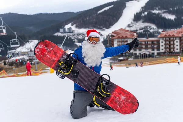 Noel Baba şapkalı bir adam kayak merkezinde snowboard yapıyor..