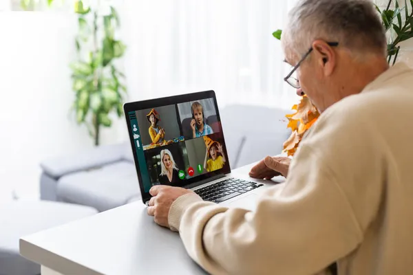 Όμορφος γέρος ντυμένος με απλό επίσημο στυλ χρησιμοποιώντας φορητό υπολογιστή, ενώ κάθεται στον καναπέ στο σπίτι. Ο ευτυχισμένος παππούς επικοινωνεί με εγγόνια. Έννοια βιντεοκλήσης. — Φωτογραφία Αρχείου