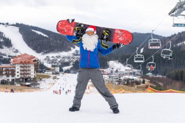 Noel Baba şapkalı bir adam kayak merkezinde snowboard yapıyor..