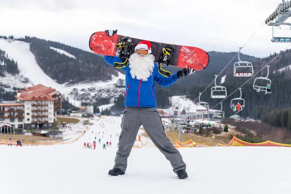 Homem de chapéu de Papai Noel com um snowboard em uma estância de esqui. — Fotografia de Stock