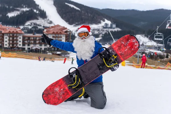 Homem feliz em santa chapéu de Natal vermelho com snowboard no inverno montanhas colina — Fotografia de Stock