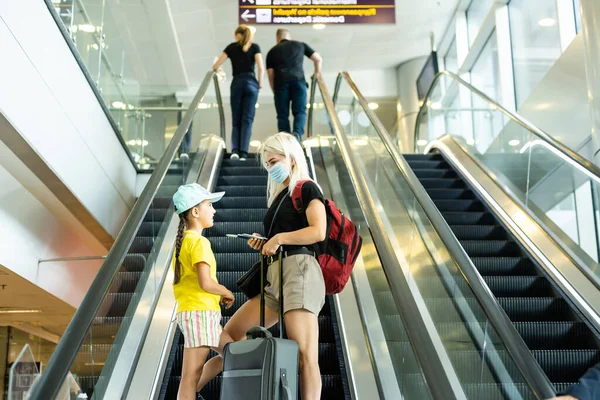 Mother with daughter going on holiday, wearing face masks at the airport. — Stock Photo, Image