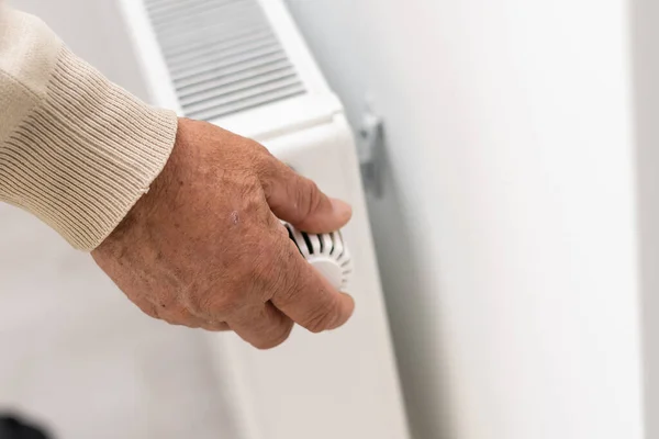 Egy idős ember megdermedt a kezében, egy férfi felmelegíti a kezét egy fűtés radiátor közelében egy lakásban, egy férfi megfagy egy lakásban.. — Stock Fotó