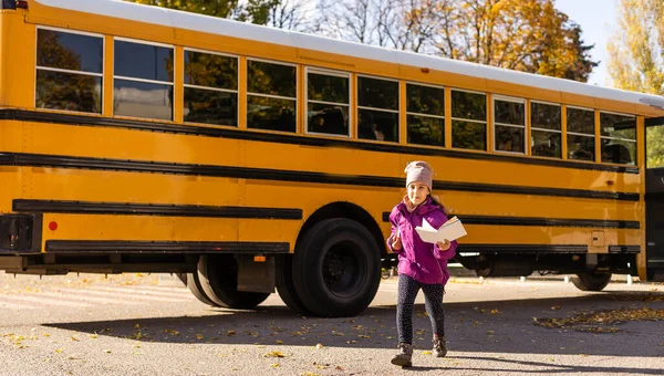 Egy kislány áll egy nagy iskolabusz mellett a könyveivel.. — Stock Fotó