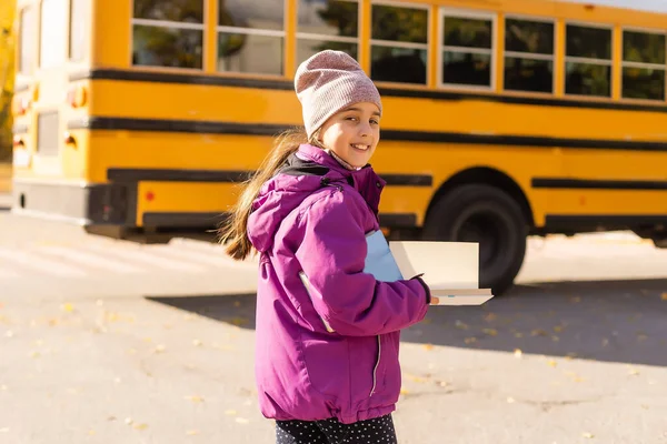 Menina em pé perto de um ônibus grande escola com seus livros. — Fotografia de Stock