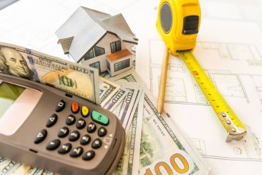 İnşaat planları, hesap makinesi, para ve kulübenin planı. Kendi evini geçindirmenin bedeli. Mülkün fiyatı. İpotek kredisi. Emlak kredisinin teminatı.