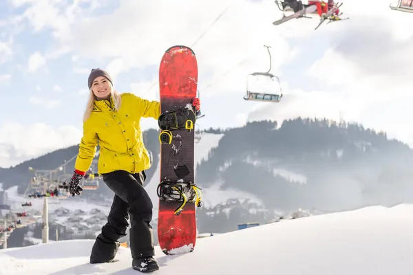 Mujer joven sosteniendo snowboard en el resort de invierno —  Fotos de Stock