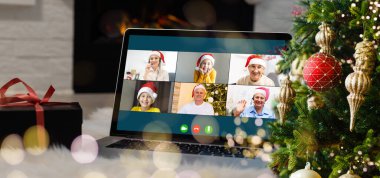 Noel selamları çevrimiçi. Beyaz kazaklı ve kırmızı şapkalı bir kadın arkadaşlarına, ailelerine ve online alışveriş için bilgisayar kullanıyor.