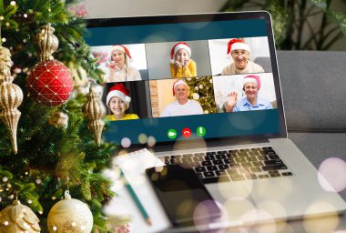 Noel selamları çevrimiçi. Beyaz kazaklı ve kırmızı şapkalı bir kadın arkadaşlarına, ailelerine ve online alışveriş için bilgisayar kullanıyor.