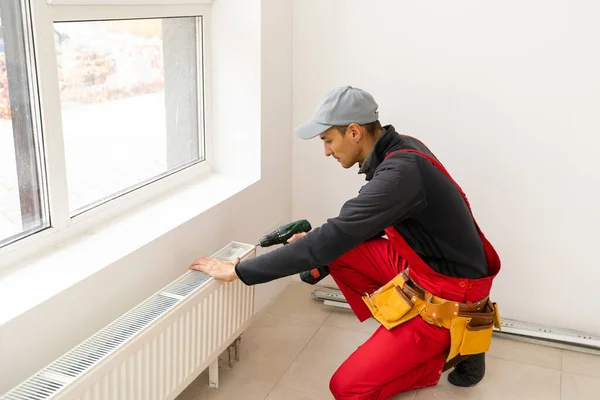 Arbetare montering vatten värme radiator nära fönstret i vitt renoverat vardagsrum, Bild med kopia utrymme — Stockfoto