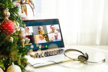 Noel selamları çevrimiçi. Beyaz kazaklı ve kırmızı şapkalı bir kadın arkadaşlarına, ailelerine ve online alışveriş için bilgisayar kullanıyor.