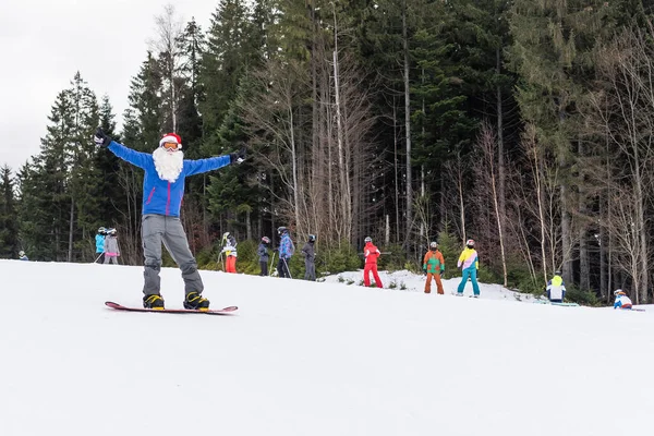 Egy férfi télapó kalapban, snowboarddal a síközpontban. — Stock Fotó
