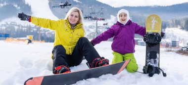 Bir dağ evinde snowboard yapan anne ve kız.