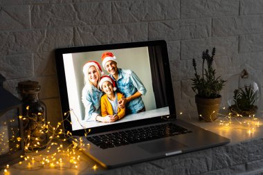 Mutlu ebeveynler kucak kucak açan şirin küçük kız hediye tutuyor. Noel hediyesini web kamerasına veriyor. Sanal aile toplantısı sırasında. Video konferansında..