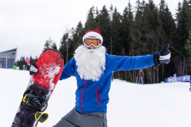 Kış Dağları tepesinde kar kayağıyla Noel Baba şapkalı mutlu bir adam.