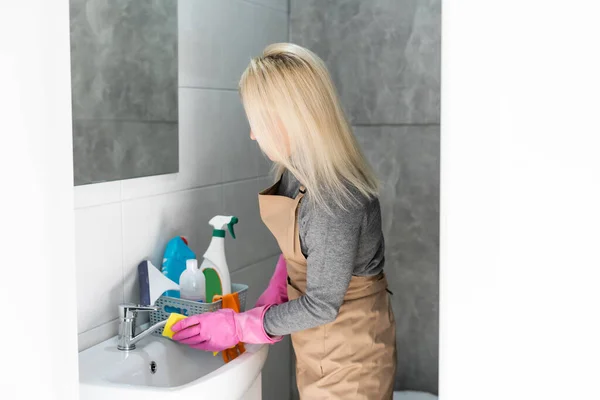 Vrouw doen klusjes in badkamer thuis, wastafel en kraan met spray wasmiddel te reinigen. — Stockfoto
