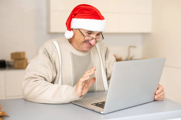 Anciano caballero celebrando la Navidad en línea en el ordenador portátil haciendo videollamada con la familia distante sentado en la cocina en casa. Vacaciones de Año Nuevo — Foto de Stock