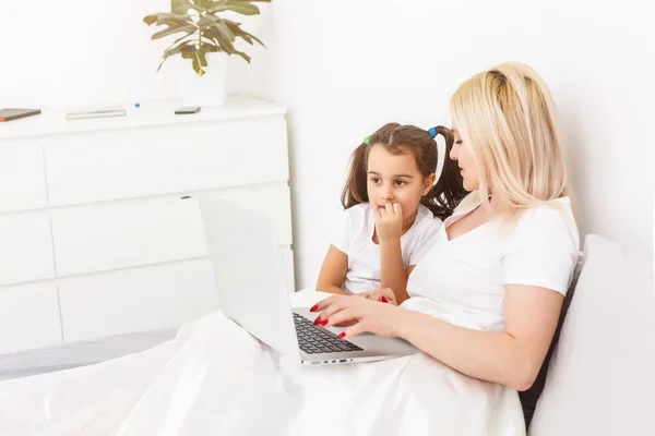 Sorridente madre e figlia utilizzando il computer portatile a letto a casa — Foto Stock