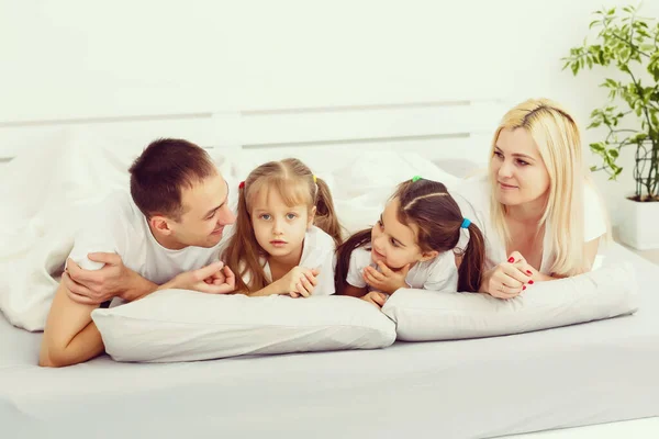 Kinderen en ouders rusten 's morgens in bed. Ze verwennen zich, knuffelen. Een tweeling. dochters. — Stockfoto