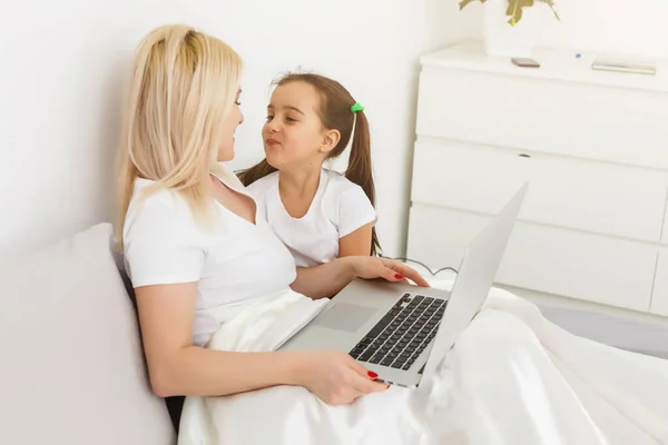 Sorridente madre e figlia utilizzando il computer portatile a letto a casa — Foto Stock