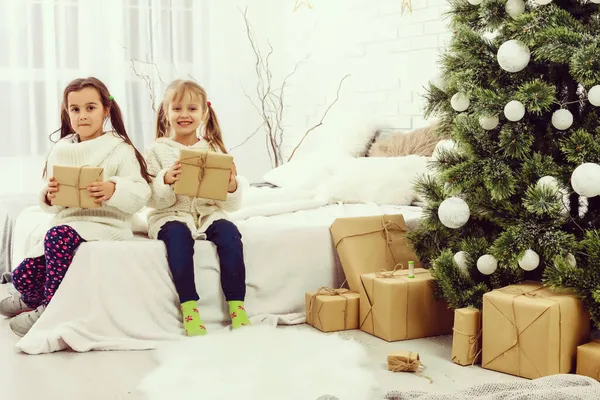Twee meisjes in de voorkant van kerstboom met geschenken en open haard — Stockfoto