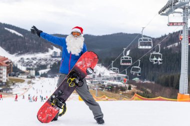 Kış Dağları tepesinde kar kayağıyla Noel Baba şapkalı mutlu bir adam.