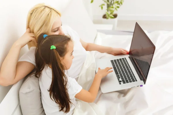 Sorridente madre e figlia utilizzando il computer portatile a letto a casa — Foto Stock