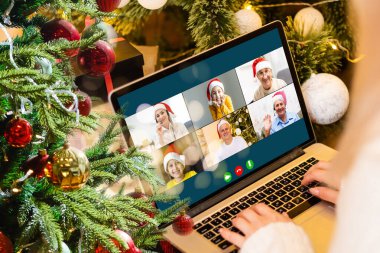 Noel selamları çevrimiçi. Beyaz kazaklı ve kırmızı şapkalı bir kadın arkadaşlarına, ailelerine ve online alışveriş için bilgisayar kullanıyor.