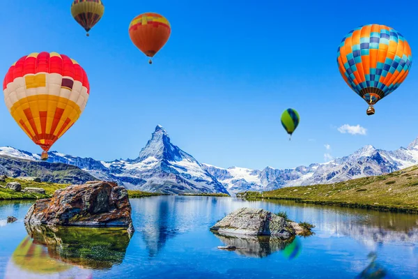 Kleurrijke heteluchtballonnen die over het meer vliegen, omringd door bergen. grote veelkleurige ballonnen die langzaam opstijgen tegen de blauwe lucht. Reizen, avontuur, festival. — Stockfoto