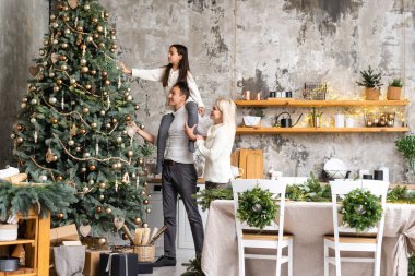 Mutlu Noeller ve mutlu tatiller. Anne, baba ve kız Noel ağacı süslüyorlar..