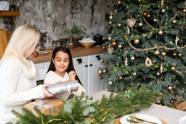 Güzel anne-kız eğleniyor, sarılıyor ve öpüyor. Beyaz bir iç mekanda Noel ağacının yanında. Aile mutluluğu, tatil, eğlence, tatil, bir kadınla oyunlar. Yeni yıl hazırlıkları