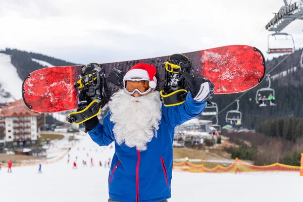 Chapeau homme au Père Noël avec un snowboard dans une station de ski. — Photo