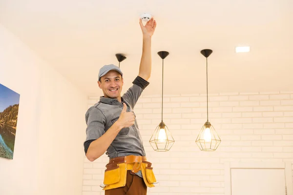 Jeune électricien installant un détecteur de fumée au plafond — Photo